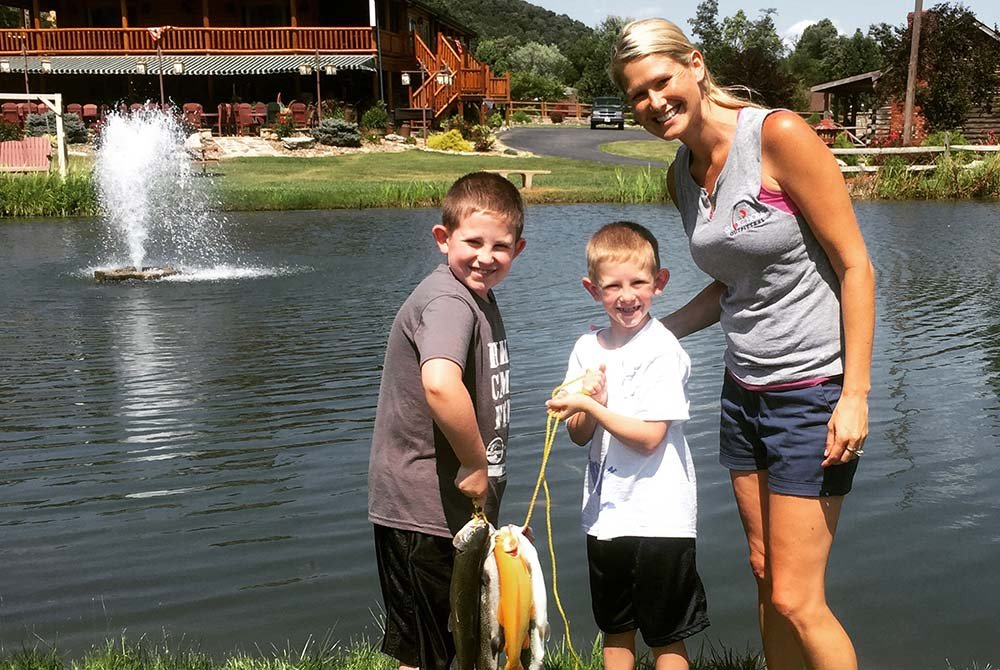 Woman and young boys holding up a line of fish by lake